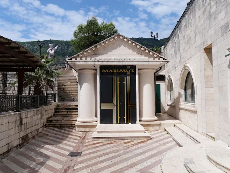 The classical-style entrance of Maximus nightclub in Kotor, with stone columns and an imposing black door.