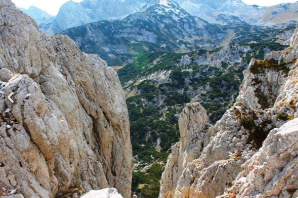 A breathtaking view through a rocky mountain pass in Durmitor, looking down into a green valley with snow-capped peaks in the distance.