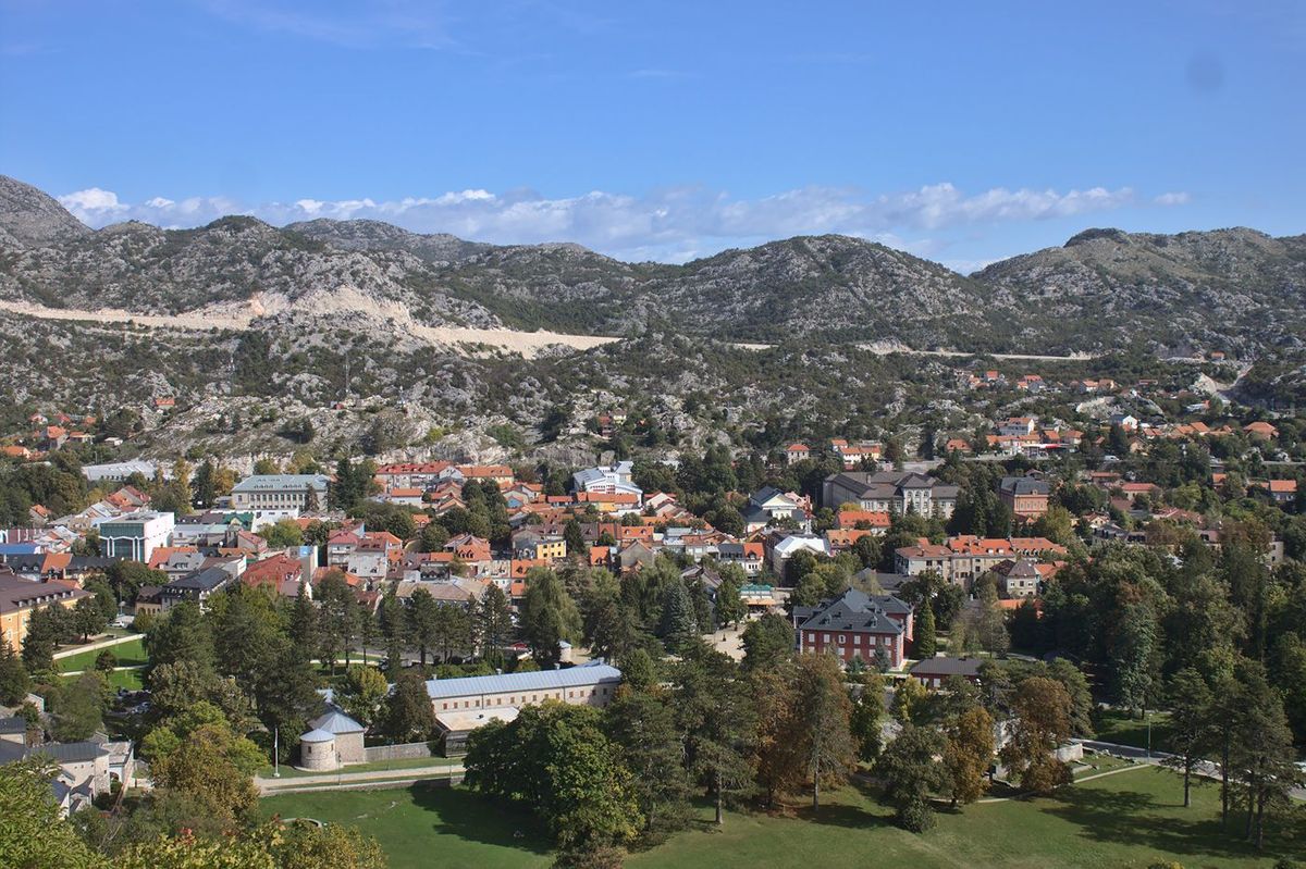  A high-angle view of Cetinje, the historic capital of Montenegro, nestled in a green valley and surrounded by rugged, grey karst mountains