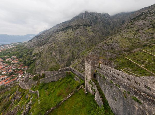 A view from the stone ramparts of St. John's Fortress as they climb the steep, rocky mountain high above the town of Kotor, with the peak in the clouds