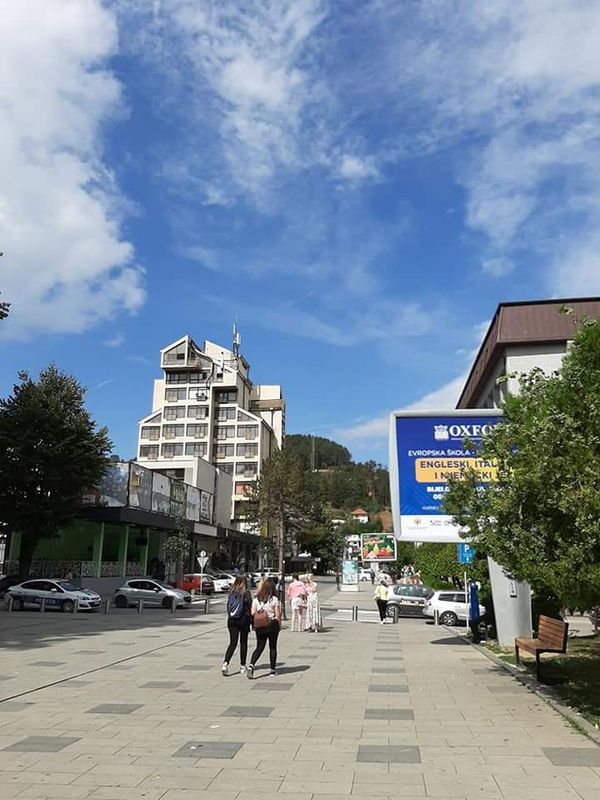 People walking on the main pedestrian street in the center of Bijelo Polje, Montenegro, with the distinctive modernist-style Hotel Bijela Rada in the background on a sunny day