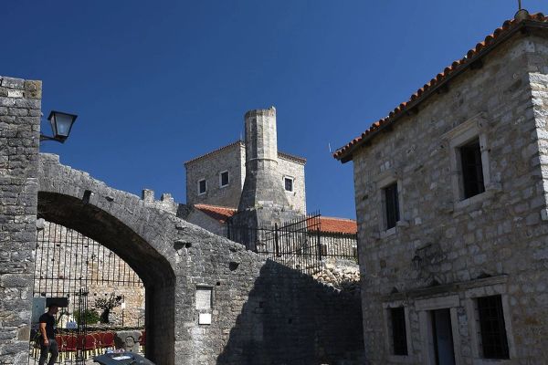 A view from within the Old Town of Ulcinj, Montenegro, showing a stone archway, historic buildings, and a tower against a clear blue sky