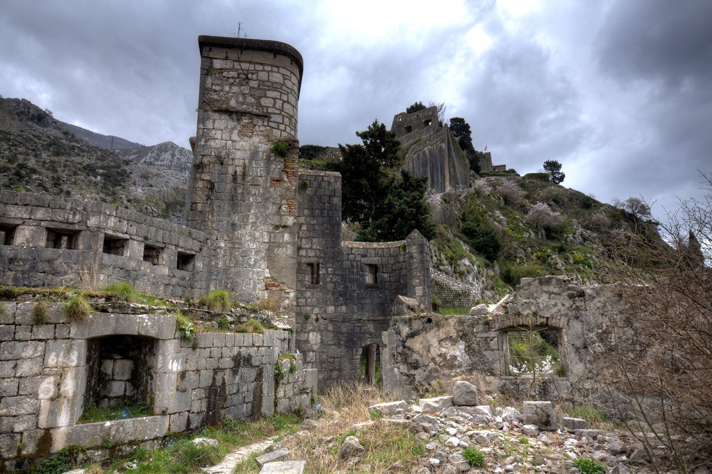 The crumbling stone ruins of St. John's Fortress in Kotor, with dramatic grey clouds overhead.