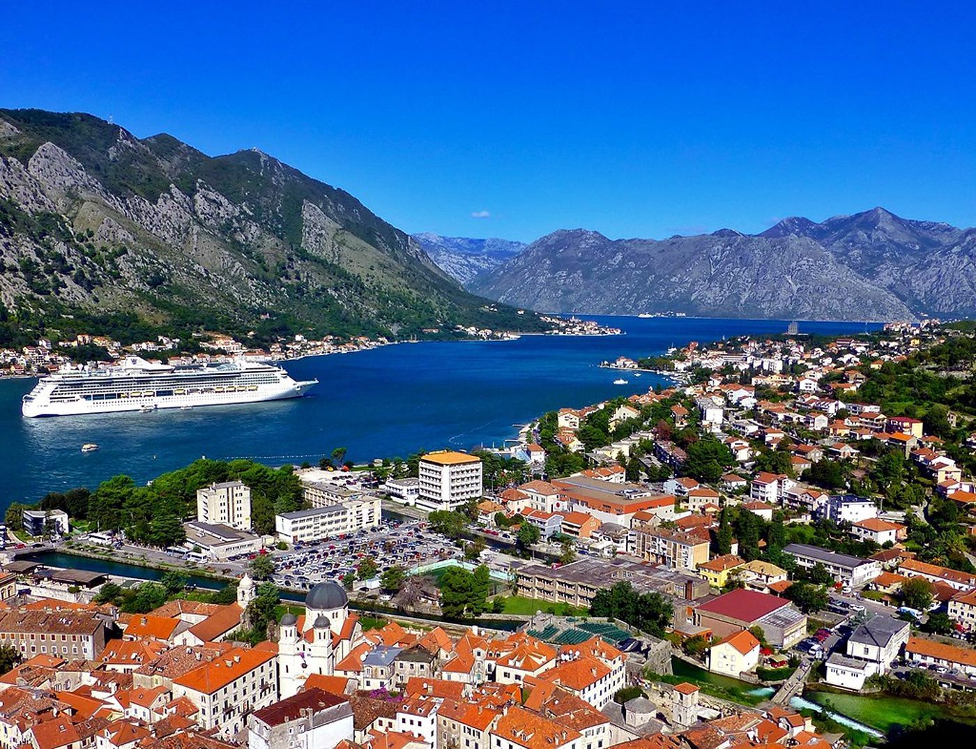 Panoramic view of the Bay of Kotor, Montenegro, with a large cruise ship on the water and the red-roofed Old Town in the foreground