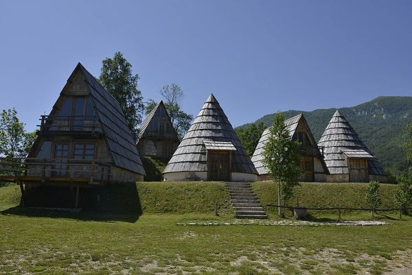A group of traditional cone-shaped and A-frame wooden huts of an ethno village in Durmitor National Park, Montenegro, on a grassy hill with a mountain in the background
