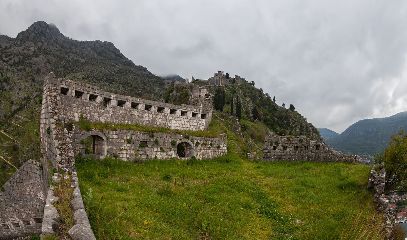 The ancient stone fortifications and city walls of Kotor snaking up the green, rugged mountainside.