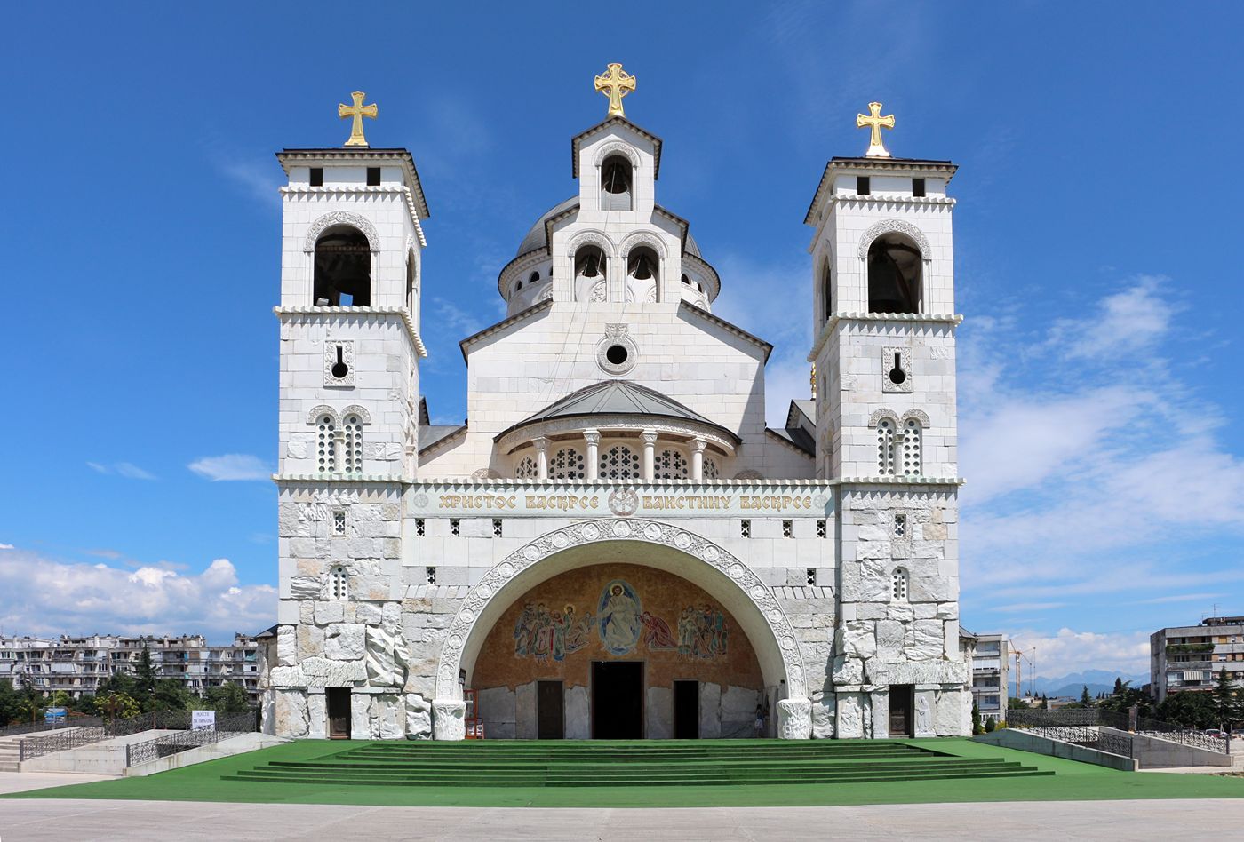 The grand facade of the Cathedral of the Resurrection of Christ in Podgorica, with its twin stone towers and golden crosses.