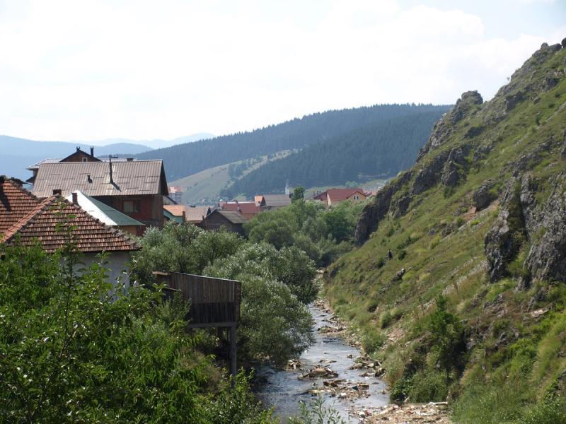 A view of the town of Rožaje, Montenegro, with traditional houses built along the rocky Ibar River, nestled in a valley of green, forested hills