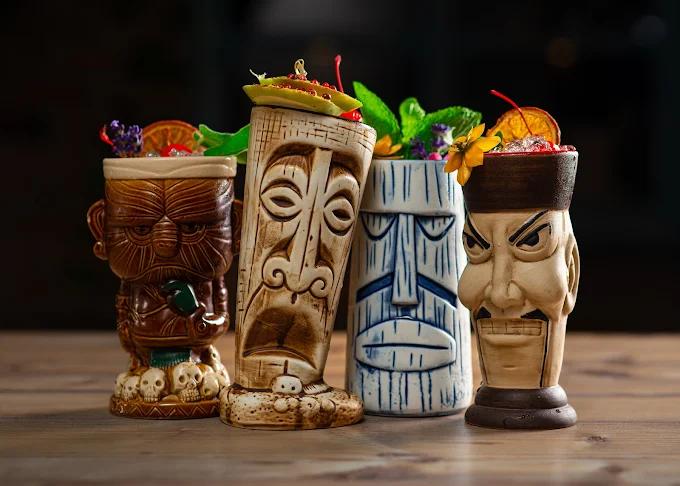A collection of four creative and exotic tiki cocktails served in unique, colorful ceramic mugs.