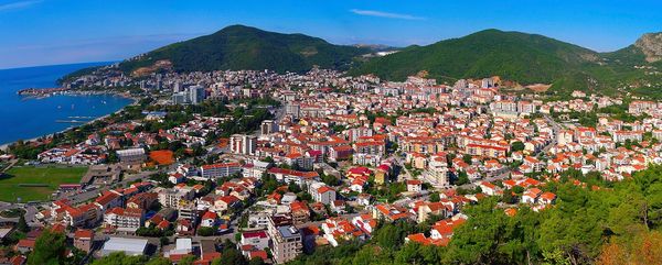 黑山布德瓦市的广角全景，城市坐落在亚得里亚海和翠绿的群山之间，上方是湛蓝的天空