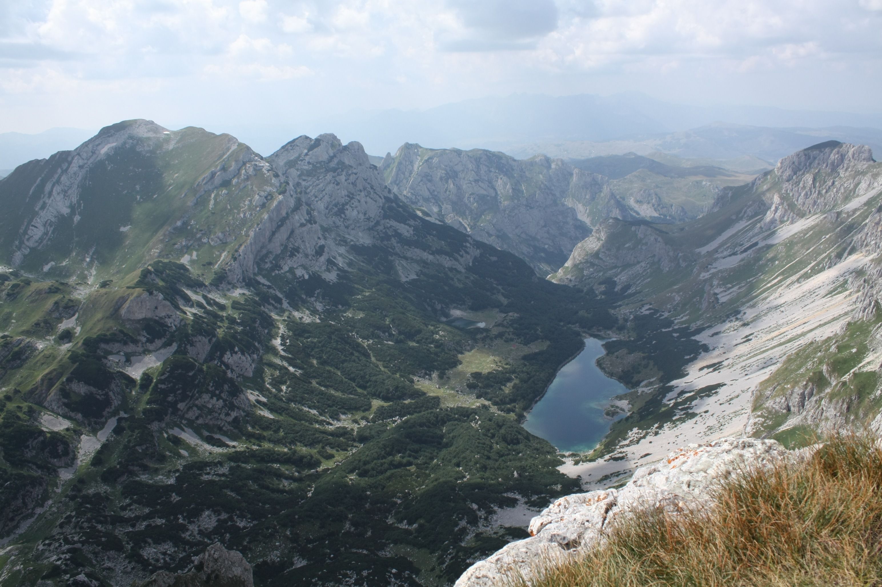 A view from a mountain peak in Durmitor, looking down into a glacial valley with a stunning alpine lake.