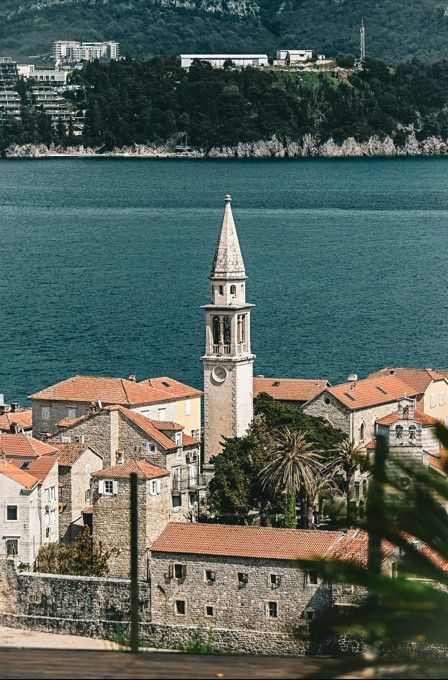The tall bell tower of the Church of Saint John rising above the red roofs of Budva's Old Town, with the Adriatic Sea behind.