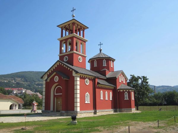 The bright red Orthodox Church of the Nativity of Christ in Mojkovac, Montenegro, with white trim, a dome, and a bell tower, seen on a sunny day