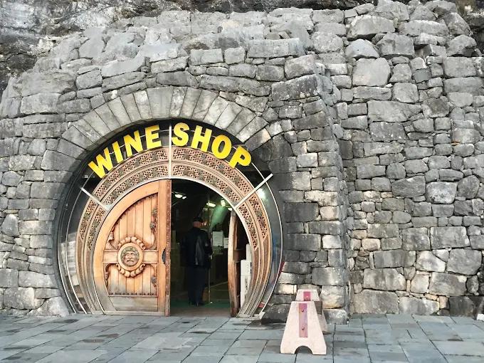 Rustic stone facade of the Plantaže Winery wine shop, with an impressive round wooden door under a 'WINE SHOP' sign.