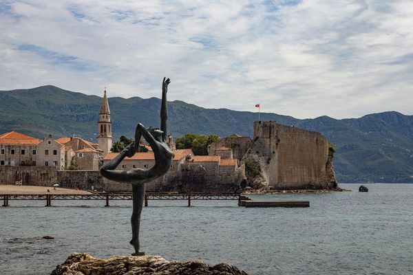 布德瓦芭蕾舞者的青铜雕像立于岩石之上，背景是黑山历史悠久的老城区和连绵的群山