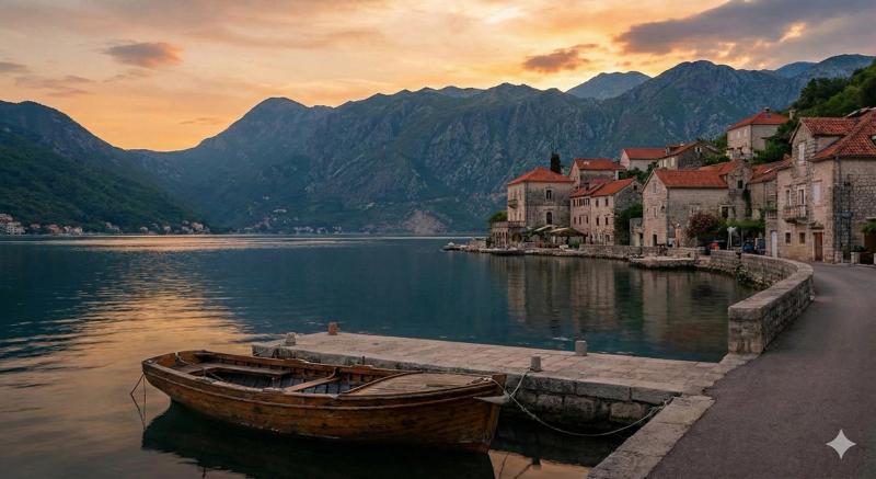 Scenic sunset view of the Bay of Kotor, Montenegro, featuring a traditional wooden boat tied to a stone pier in front of a historic waterfront village and mountains.