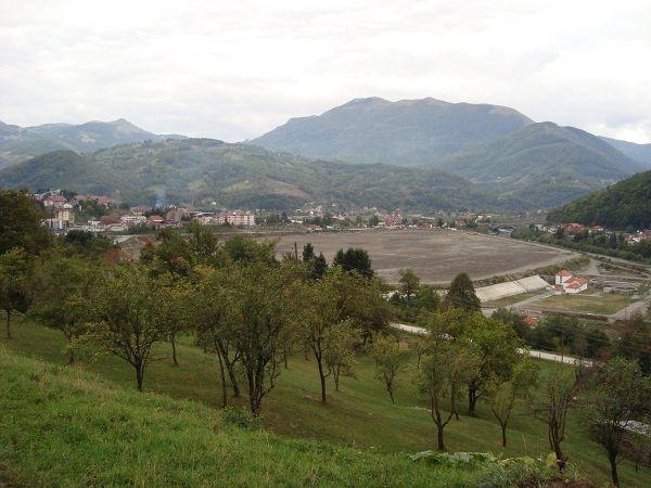 A panoramic view of Mojkovac, Montenegro, showing the town nestled in a valley next to the vast, former mine tailings pond (Jalovište), with green mountains in the background.