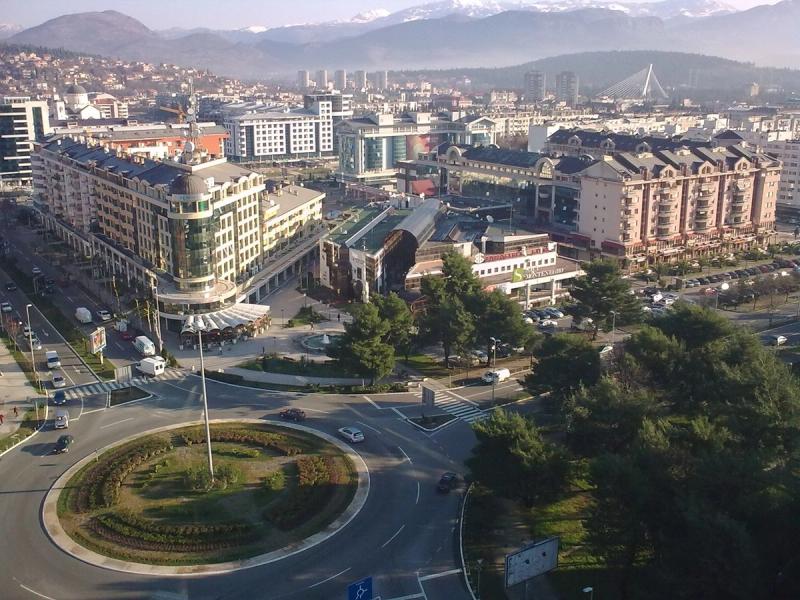 A panoramic view of downtown Podgorica, Montenegro, with the Millennium Bridge spanning the Morača River under a clear sky