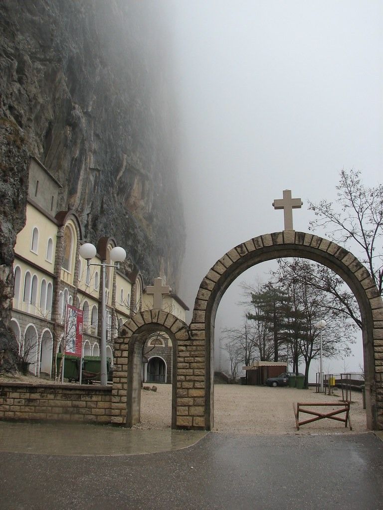 The stone entrance gates to the Lower Ostrog Monastery on a misty, atmospheric day.