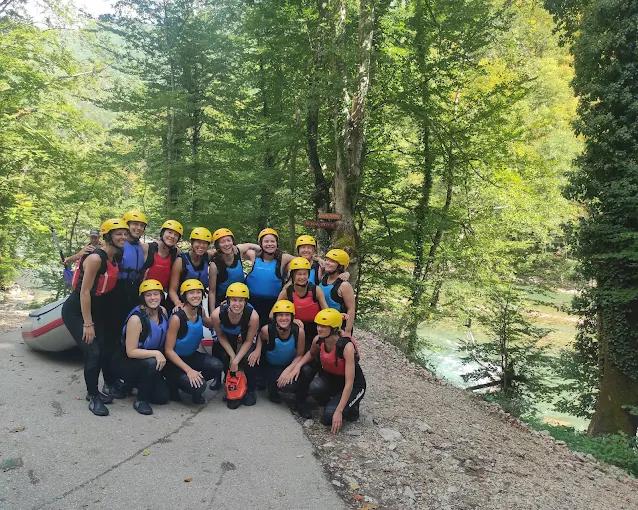 A large, happy group of rafters in full gear, smiling and posing for a photo on the banks of the Tara River before their adventure.