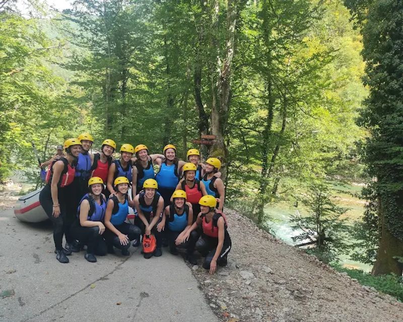 A large, happy group of rafters in full gear, smiling and posing for a photo on the banks of the Tara River before their adventure.
