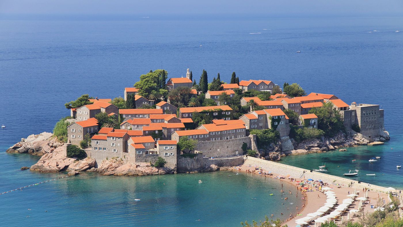 The iconic fortified islet of Sveti Stefan with its red-roofed stone houses, connected to a public beach by a narrow isthmus.