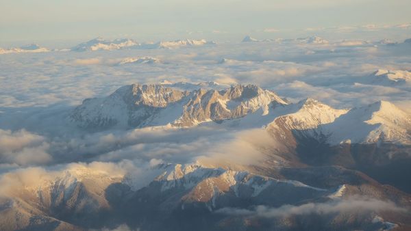 Une vue aérienne majestueuse des sommets enneigés des montagnes Komovi près de Kolašin, au Monténégro, s'élevant au-dessus d'une mer de nuages au lever du soleil