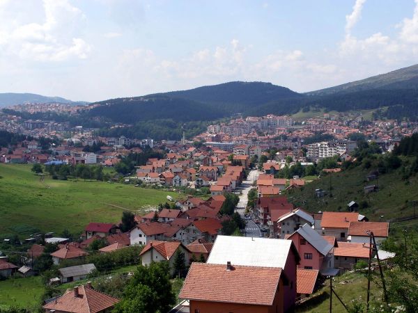 A high-angle panoramic view of the city of Pljevlja, Montenegro, nestled in a valley and surrounded by vast, rolling green hills and forests