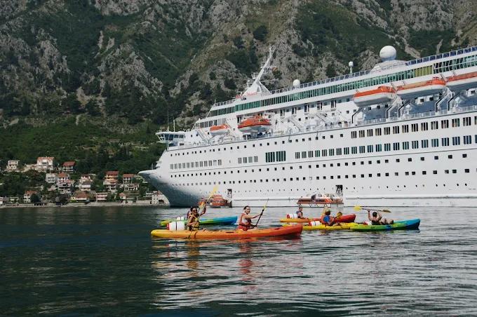 A group of kayakers paddling in the bay, passing by a large white cruise ship, showcasing the scale and beauty of the location.