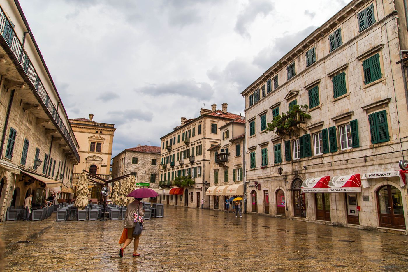 A wide view of Arms Square in Kotor's Old Town on a rainy day, with wet cobblestones and historic Venetian buildings.