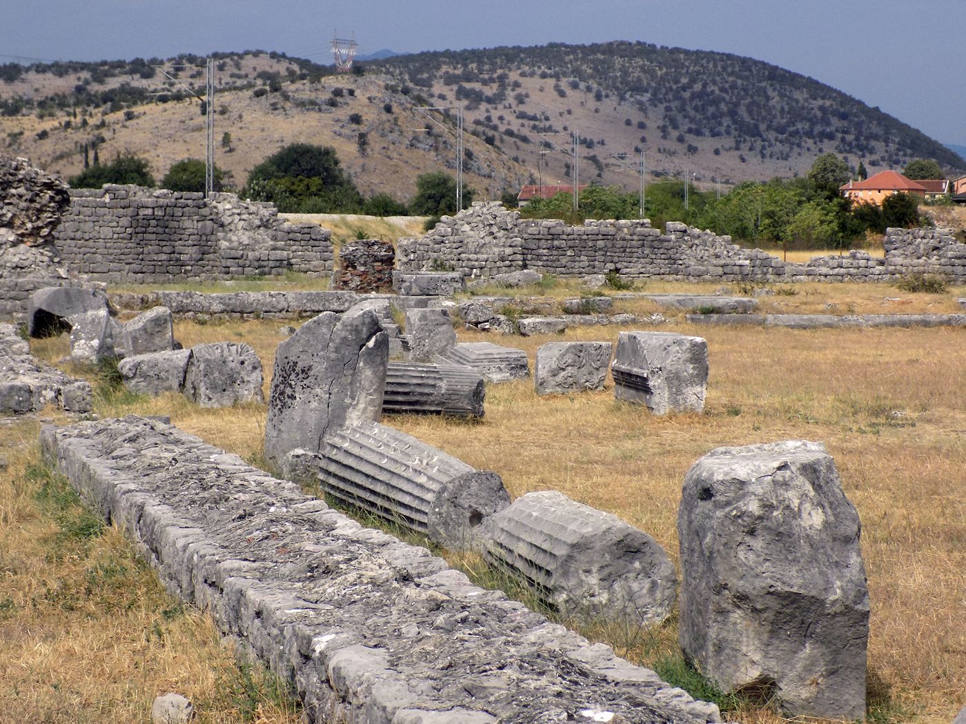 Fallen Roman columns and ancient stone foundations at the archaeological site of Doclea, with Montenegrin hills in the background.