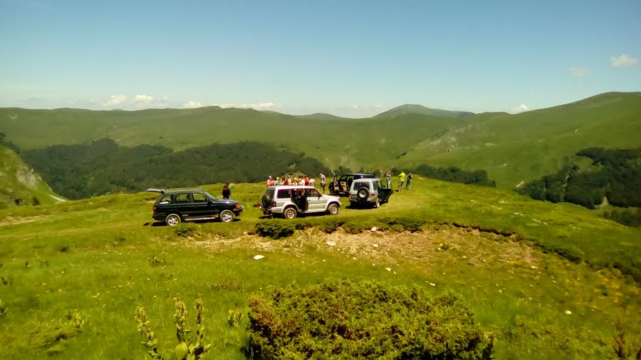 Kilka jeepów safari Sport Turist zaparkowanych na zielonym grzbiecie górskim w Kolašinie, z grupą turystów podziwiających panoramiczny widok.