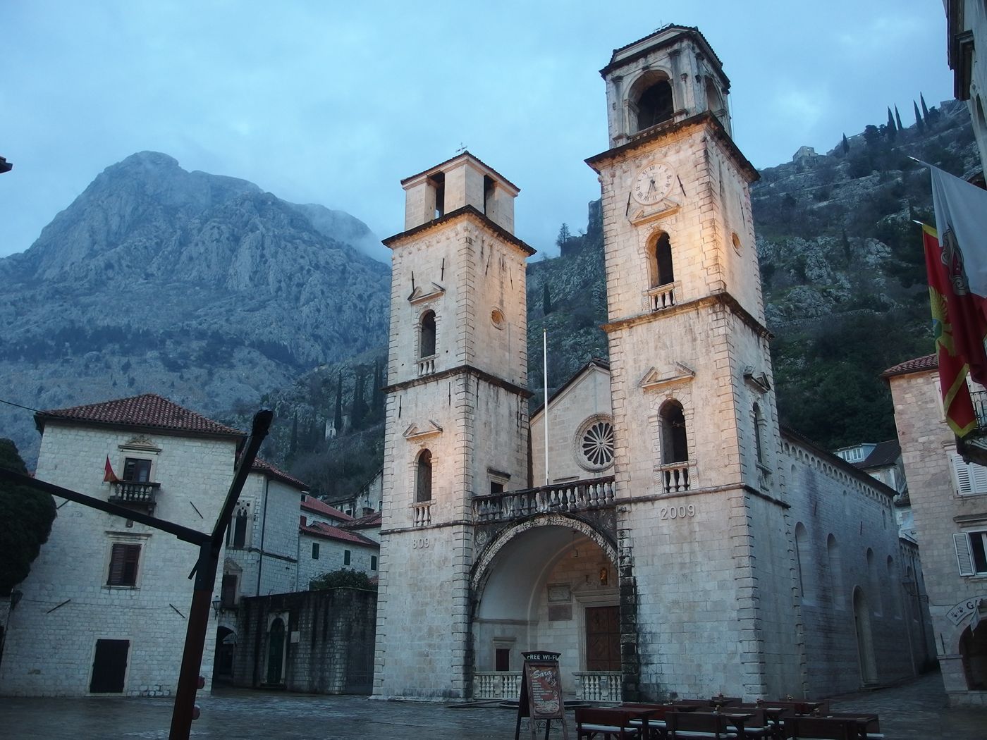 The Cathedral of Saint Tryphon at dusk, its stone facade illuminated against the dramatic backdrop of Kotor's mountains.