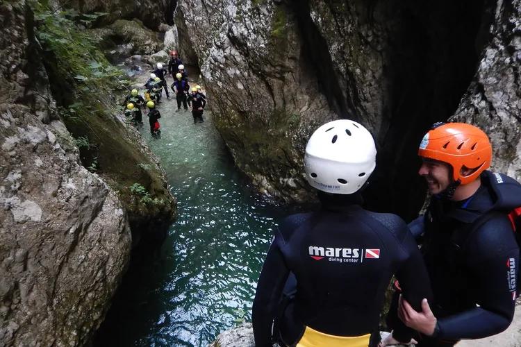 A team of adventurers in wetsuits and helmets exploring the narrow, water-filled Nevidio Canyon as part of a canyoning tour.
