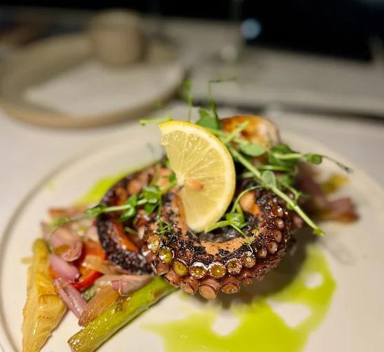 An artistically presented grilled octopus dish from Restaurant Galion, decorated with lemon and microgreens, exemplifying its modern Mediterranean cuisine.