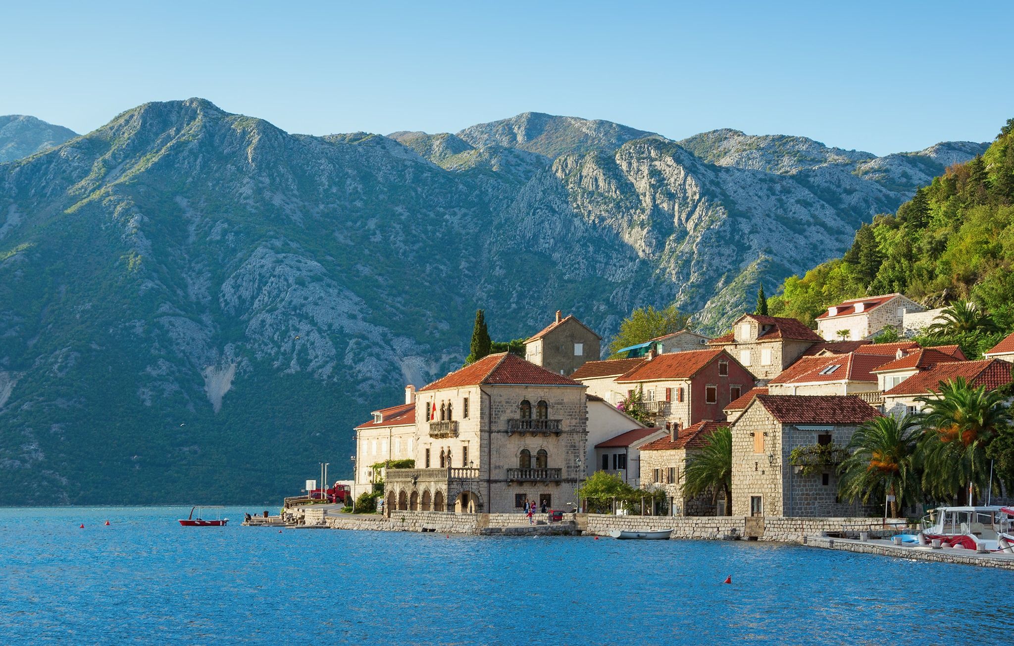 A scenic view of the historic village of Perast on the coast of the Bay of Kotor, with its stone houses and church towers against a backdrop of steep mountains.