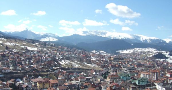 A high-angle view of the city of Rožaje, Montenegro, in early spring, with patches of melting snow on the hillsides and a backdrop of high, snow-covered mountains