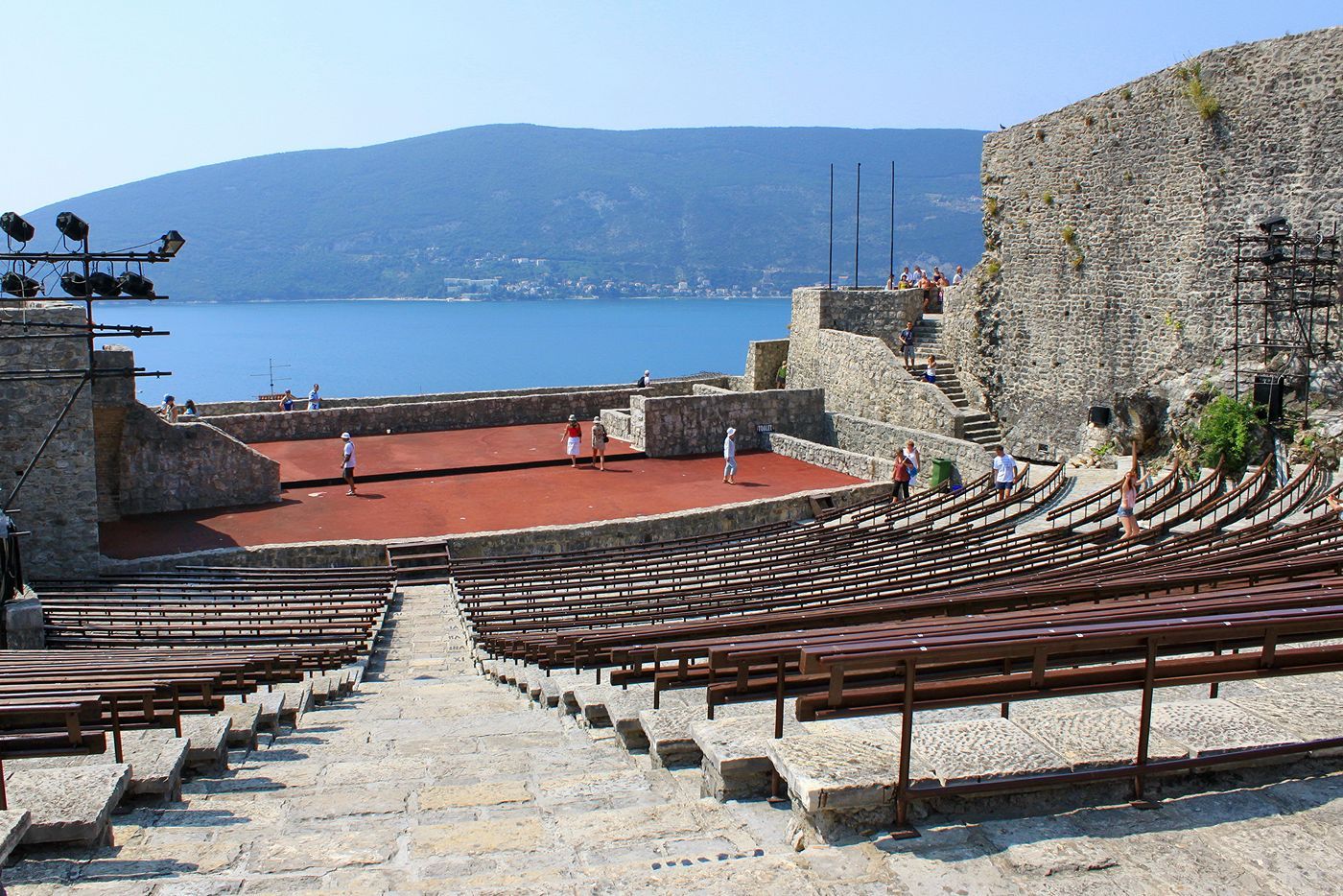 The large open-air amphitheater inside Kanli Kula Fortress in Herceg Novi, with the Bay of Kotor in the background.