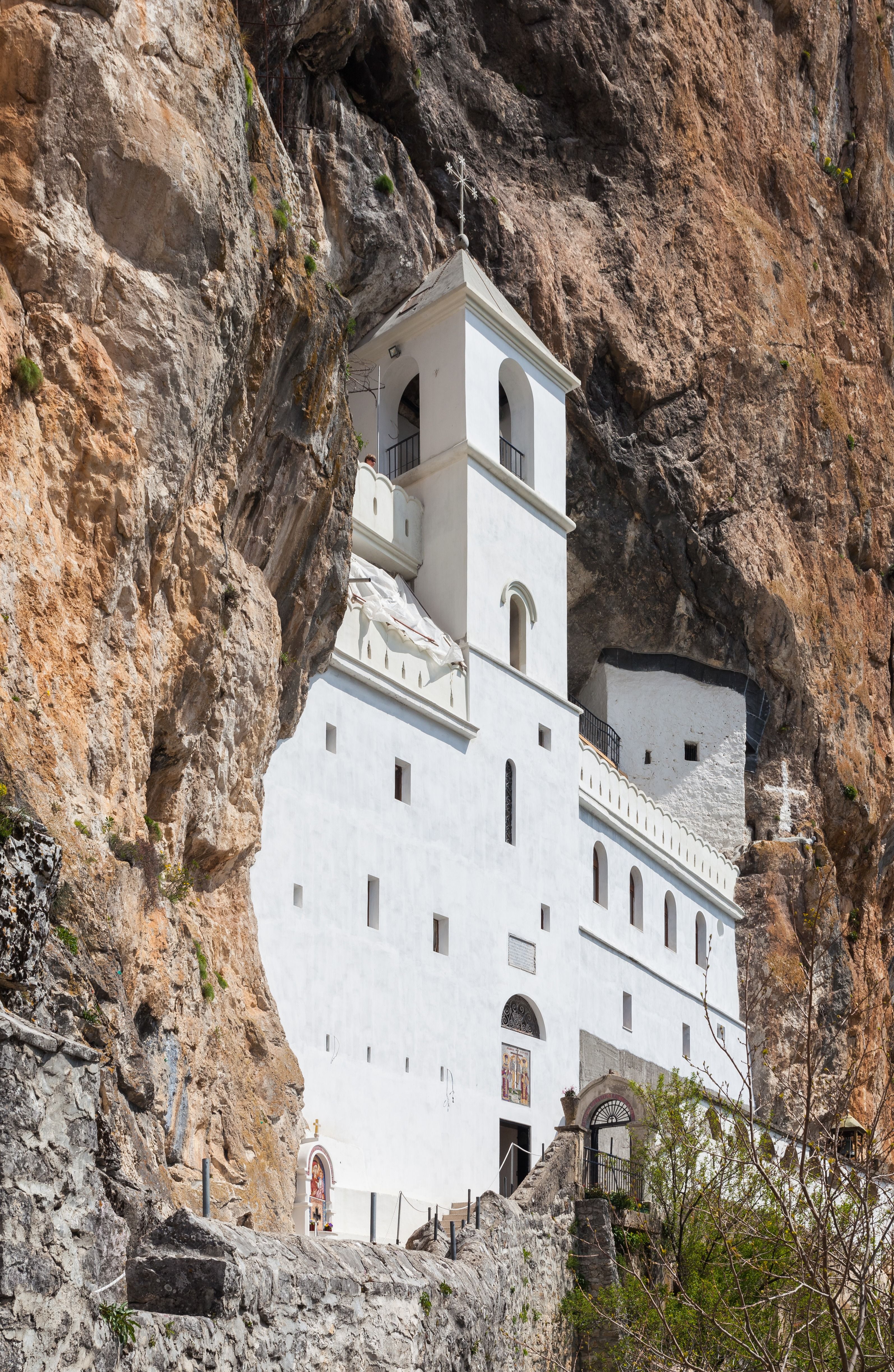 A close-up view of the white walls and bell tower of the Upper Ostrog Monastery, nestled in a rock cave.