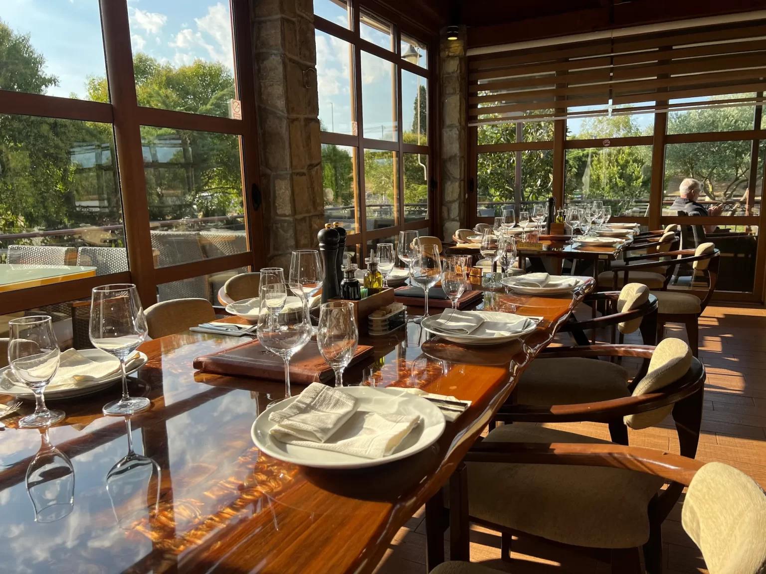 A beautifully set, long wooden dining table in the Hotel Aria restaurant, with sunlight streaming through large windows.