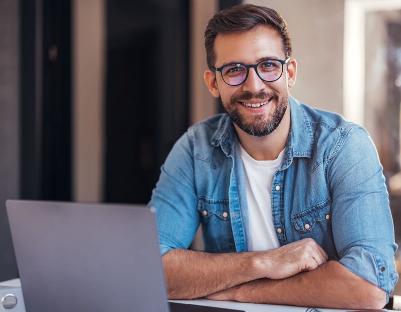 Smiling man with glasses sitting at a laptop