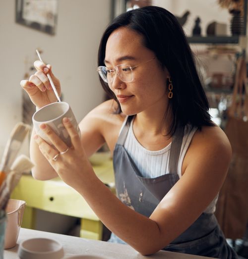 Ceramic artist painting glaze onto a handmade cup with a small brush