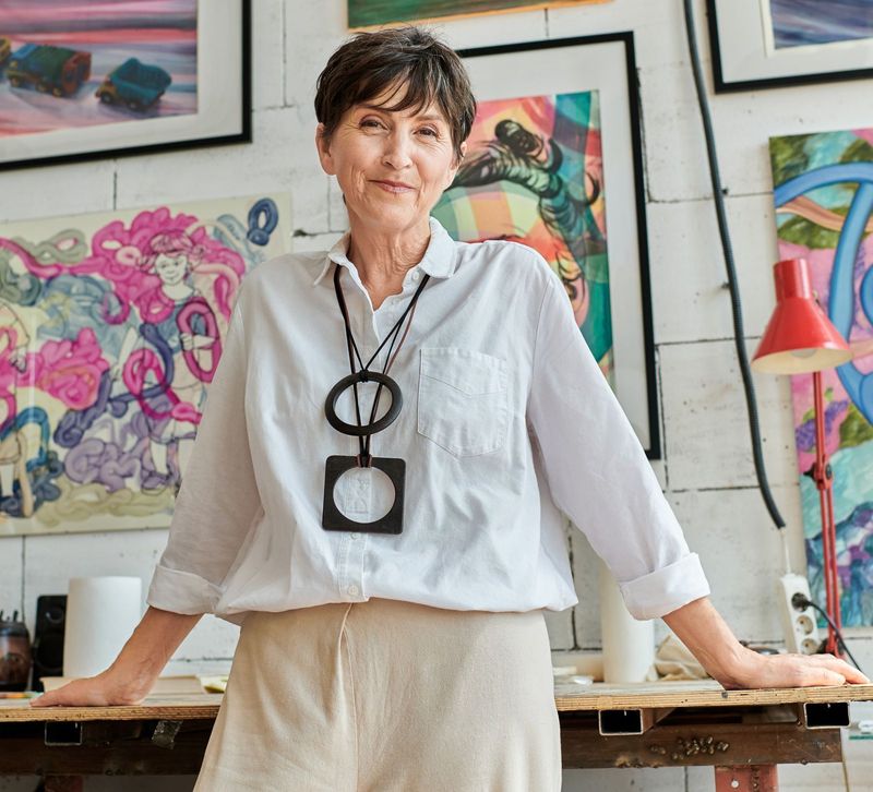 Artist standing in her studio surrounded by colorful paintings