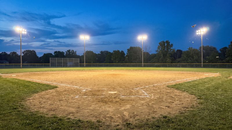 An empty youth baseball field with the lights on at dusk