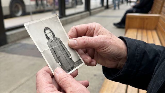 A woman's hands holding a small worn photograph of a little girl at a bus station
