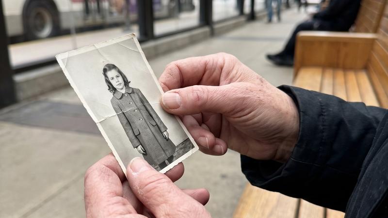 A woman's hands holding a small worn photograph of a little girl at a bus station