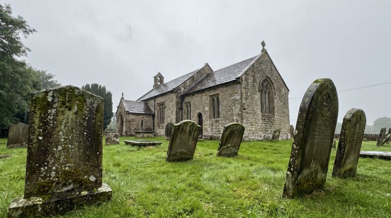 A quiet English stone churchyard under a grey drizzling sky