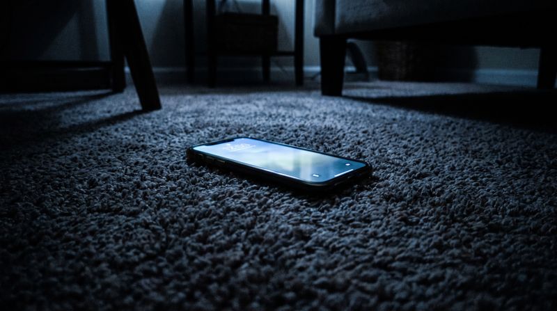 A phone lying face-up on a bedroom floor, its screen glowing in the dark