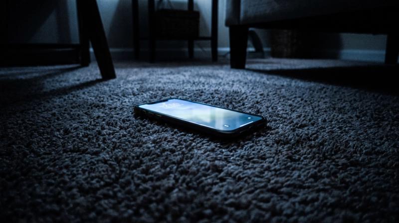A phone lying face-up on a bedroom floor, its screen glowing in the dark