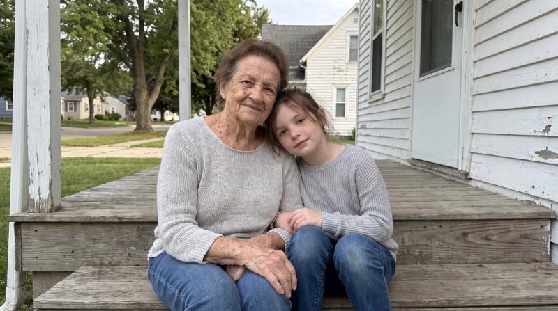 An older woman and a young girl sitting together on the front porch of a small house